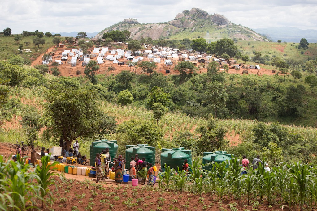 People queue outside a water storage and pump facility built by Medecins Sans Frontiers (MSF). The satellite camp of Kapise 2, less overcrowded than the main one, is in the background. The rock in the background is already beyond border between Mozambique and Malawi. <br/><br/>Over 5.800 Mozambican nationals have camped in the village of Kapise 2 in Malawi after fleeing their homes in Mozambique. The only regular water source in the village has ran dry and the only way to get water is from few pre-existing sources and the two additional boreholes respectively rehabilitated and constructed by MSF. Even then, waiting time is at times up to 2.5 hours at the water pump and with the continuous influx of people, the capacity of the borehole today can only provide around 8 liters of water per person per day, well below the minimum humanitarian standards of 15-20L. © James Oatway / MSF
