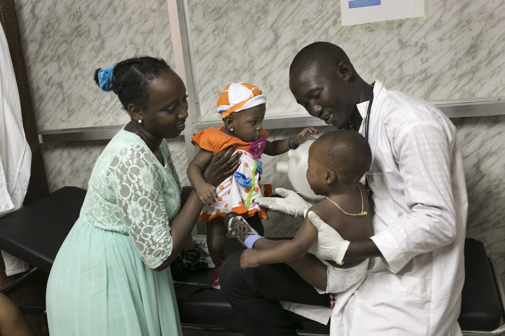 Nine month old Nubia plays with her half brother M'Bemba (14 months) during a medical consultation with Dr. Daouda Berete (r) and Medecins Sans Frontieres (MSF) Health Promoter Camara Djenab (l), herself an Ebola survivor; at the MSF facility in Nongo, Conakry. Photographer: Albert Masia