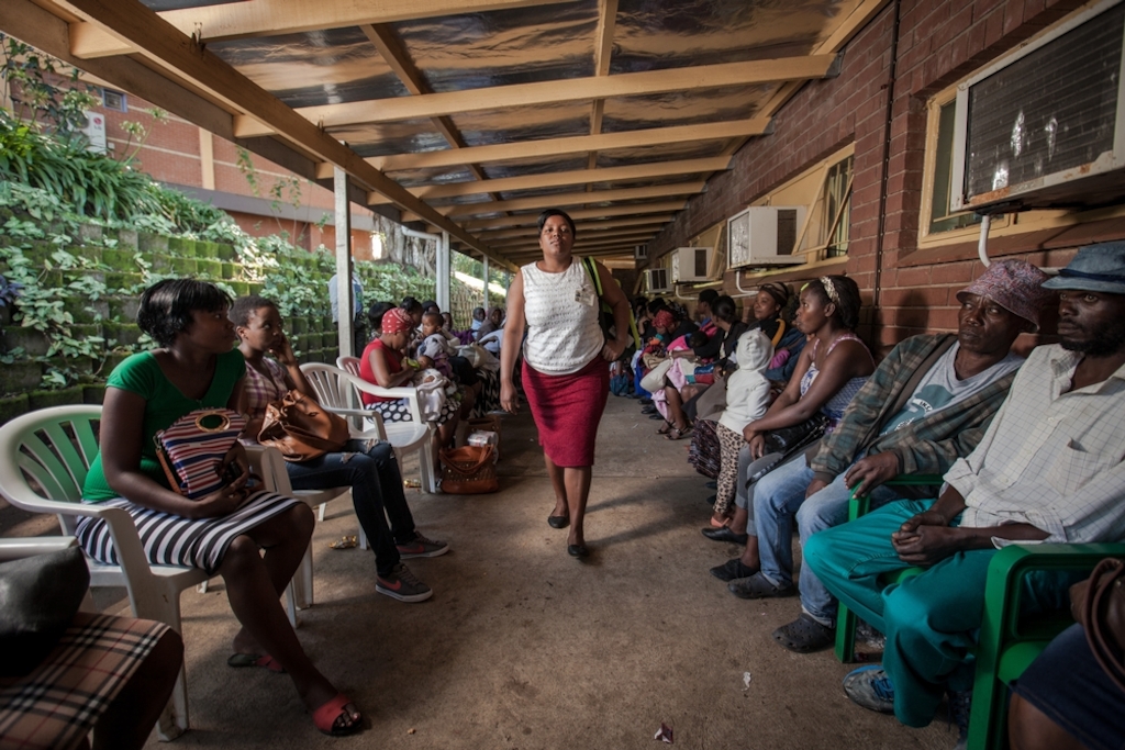 Community Care Giver Nonhlanhla Ngema passes a long queue of patients at Eshowe Gateway Clinic to pick up ARVs for members of her Community ART Group (CAG). Medecins Sans Frontieres (MSF) has been piloting CAGs as a model of care for stable HIV+ patients in rural districts of southern Africa, where HIV prevalence is at its highest. CAG members meet once every two months to review their health and arrange for collection of their ARVs without having to sit in long queues at clinics. Photographer: Greg Lomas / Médecins Sans Frontières