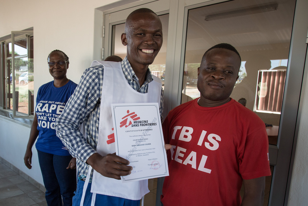 Celumusa Hlatswako (center), MSF mobile counselor, receives a sign language qualification certificate. He wanted to learn sign language to be able to communicate and help deaf MDR-TB patients. Hearing loss is one of the side effects of the MDR-TB treatment. Behind him, in the blue shirt, is Sellah Moraa, the MSF project coordinator of Matsapha clinic. Next to him, red shirt, Dr. Emmanuel Masombuko, MSF Medical Team Leader. Matsapha, Manzini Region, Swaziland. Photographer: Alexis Huguet