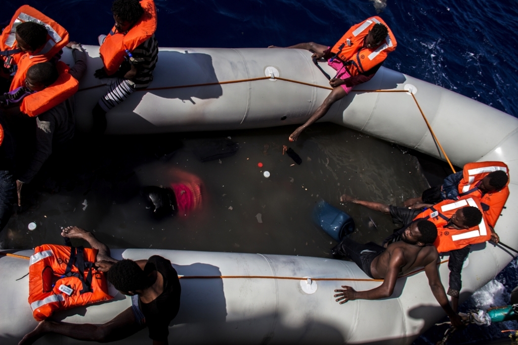 People wait to be rescued from a dinghy next to the bodies of people who died during a crossing of the Mediterranean sea. MSF teams rescued 246 people and discovered 25 dead bodies on the boat. Photographer: Borja Ruiz Rodriguez/MSF