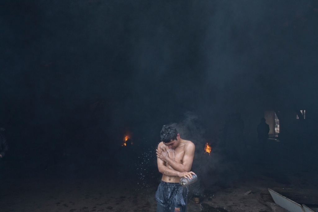 A man washes himself with hot water outside a disused railway warehouse used by refugees and migrants as temporary shelter in Belgrade, Serbia. Photographer: Marko Drobnjakovic