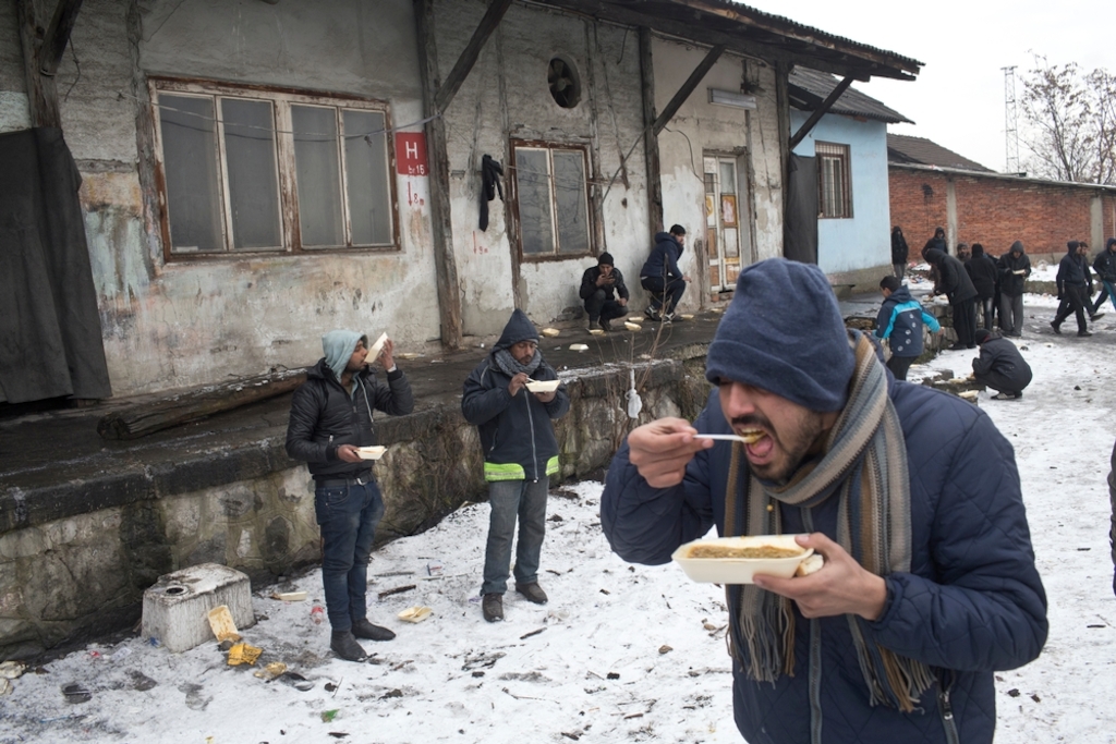 People eat meals outside an abandoned railway warehouse used as shelter by refugees in Belgrade. Photographer: Marko Drobnjakovic