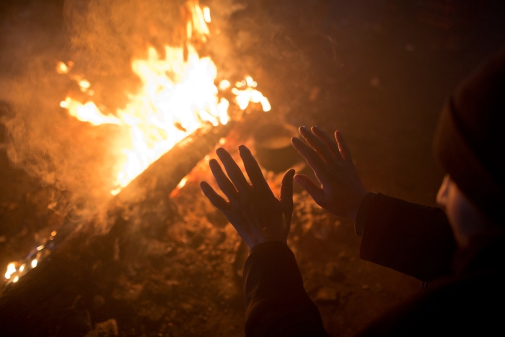 A man warms his hands by a fire inside an abandoned warehouse used by refugees as shelter in Belgrade, Serbia. Photographer: Marko Drobnjakovic