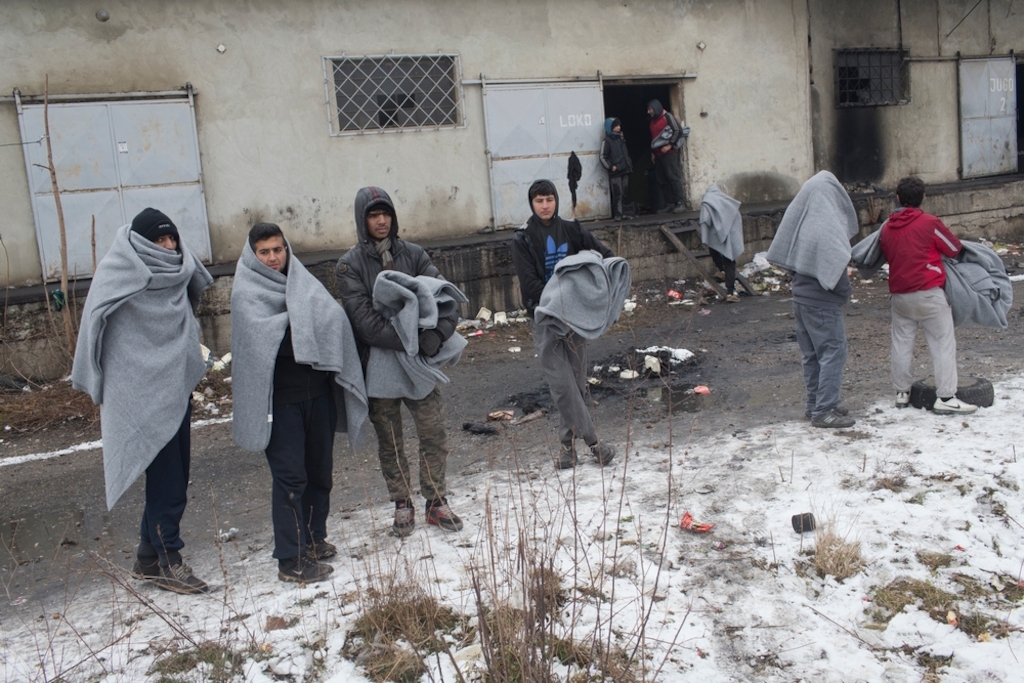 Refugees wrapped in blankets stand in front of an abandoned warehouse in Belgrade, Serbia. Photographer: Marko Drobnjakovic