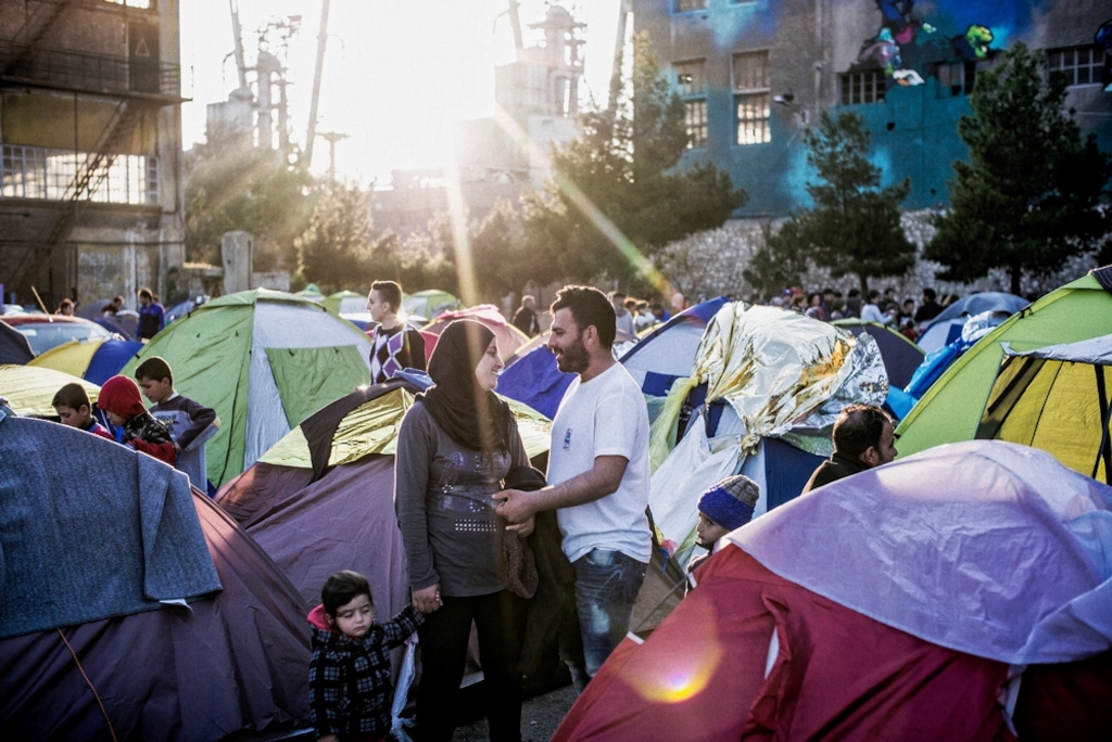 A couple share a moment in the sunlight in a makeshift refugee camp set up in the shadow of the docks in Piraeus, near Athens. Some 5,000 people who intended to travel north found themselves stuck in the Greek capital when the Former Yugoslav Republic of Macedonia closed its borders in March. Photographer: Guillaume Binet/MYOP