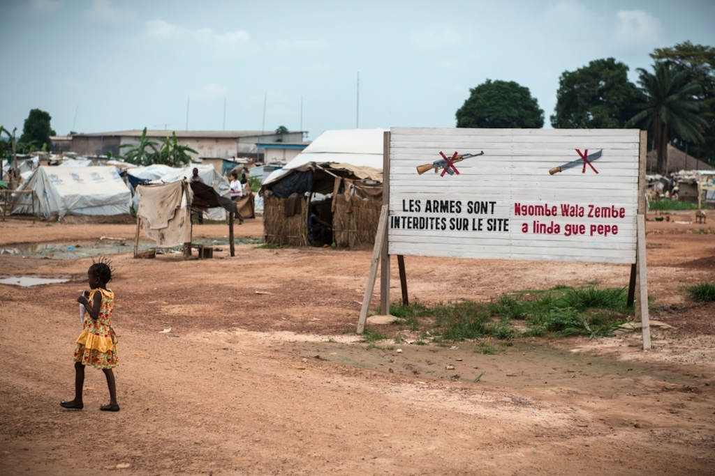 Girl near "no weapon" sign in Mpoko IDP camp at Bangui International Airport. Photographer: Yann Libessart/MSF