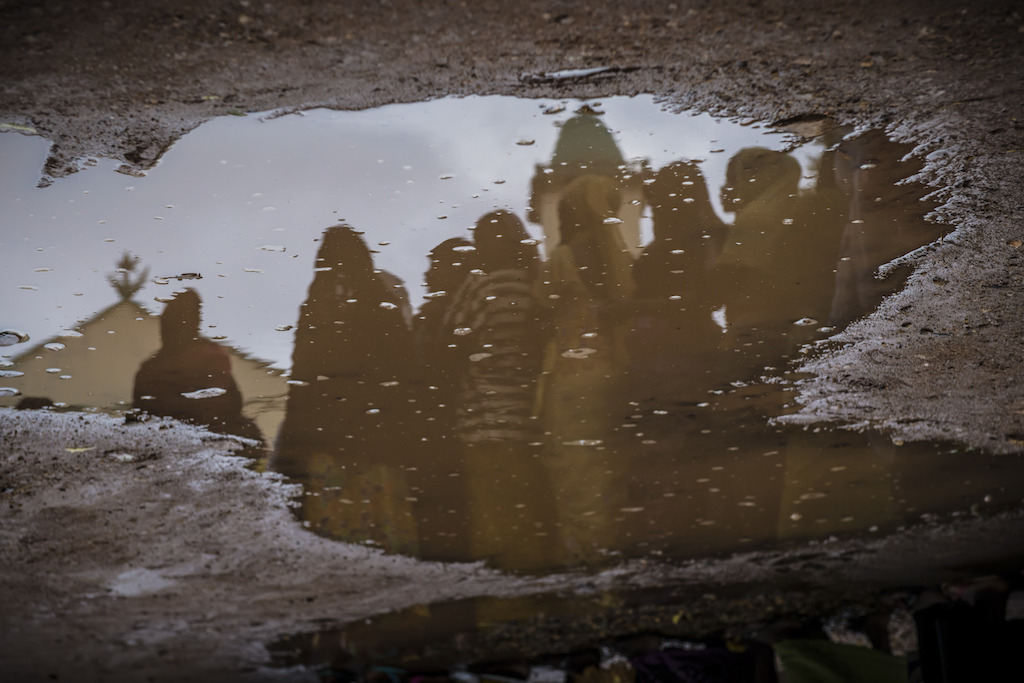 IDP women reflecting in a puddle near water distribution point at Mpoko MSF hospital. Photographer: Yann Libessart
