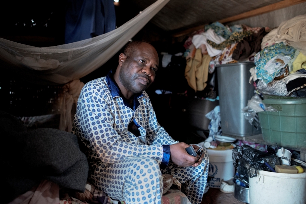 MSF159881<br/>Portrait of Valentin, at a displaced persons camp in M'Poko, Bangui.<br/><br/>"There are twelve people in this shelter. In the evening, we put a mattress on the floor and sleep next to each other. It's cold at night but fortunately an NGO gave us blankets a few days ago."<br/><br/>Valentin is a civil administrator. He lives in Mpoko camp near the airport in Bangui but is originally from PK5 district of Bangui. He fled his neighbourhood on December 5 following an outbreak of violence. Armed men came and killed two of his neighbours and one of his sons (Arthur, 38), and then they looted the house. Valentin had to bury his son in the plot of land that he owns because it was too dangerous to go to the cemetery. He then fled his neighbourhood to go to Mpoko camp. It took several days before he could meet his family again, as they had all been hiding in different places. With his wife, nine children (the youngest is 4 years old and the oldest 24 years old) and six grandchildren, they all slept outside in the camp when they first arrived: "It was raining and we had to sleep outside. <br/><br/>With the salary of Valentin, the children can go to school and university and the family can live a better life than some other families in the camp, but that is still not enough to feed everyone. "After the Pope's visit, it felt like there was a wave of solidarity amongst the population but is that enough to maintain security?" Valentin wants the rapid disarmament of armed groups that are, according to him, the origin of the trouble in the country. "The presidential elections offer hope. We hope whoever is elected will be respected by all. "