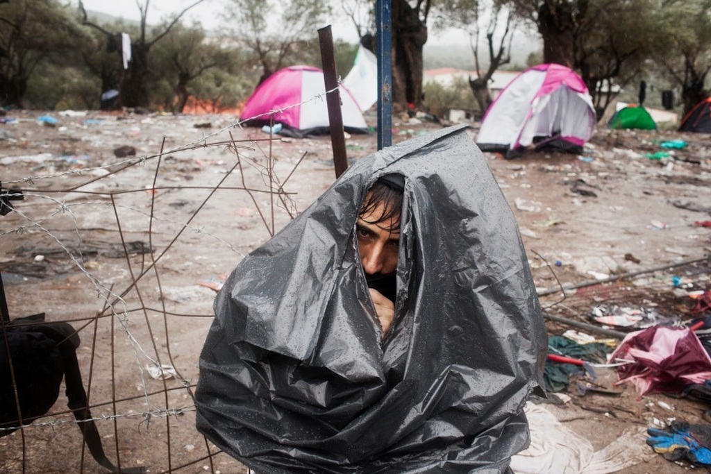 Photographer: Alessandro Penso<br/><br/>Caption: An Afghan refugee wears a rubbish bag to keep himself dry during a rainstorm at the Moria Reception Centre while he waits for his documents on the island of Lesbos.