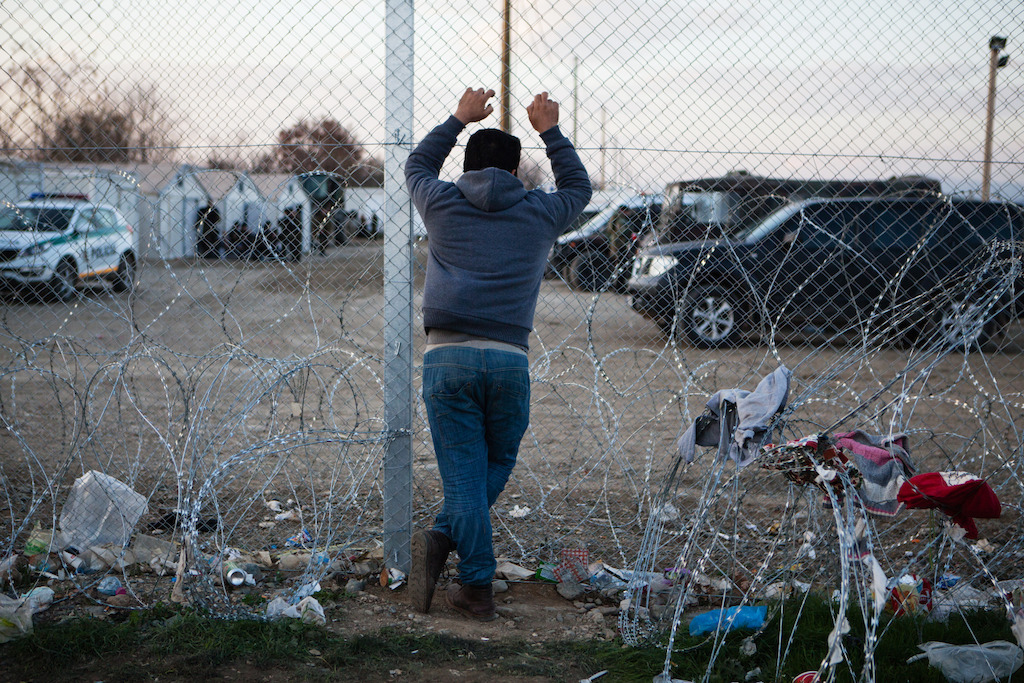 A man looks through the border fence into Macedonia (FYROM). Photographer: Alex Yallop