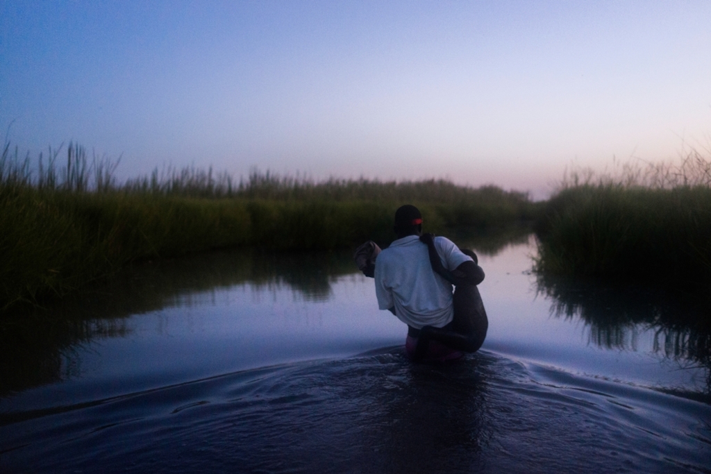 Wading at dusk through the swamplands of Unity state, an MSF staff member carries a young boy as his family make their way to the relative safety of Kok island, where more than 2,000 people are sheltering from conflict. Photographer: Dominic Nahr
