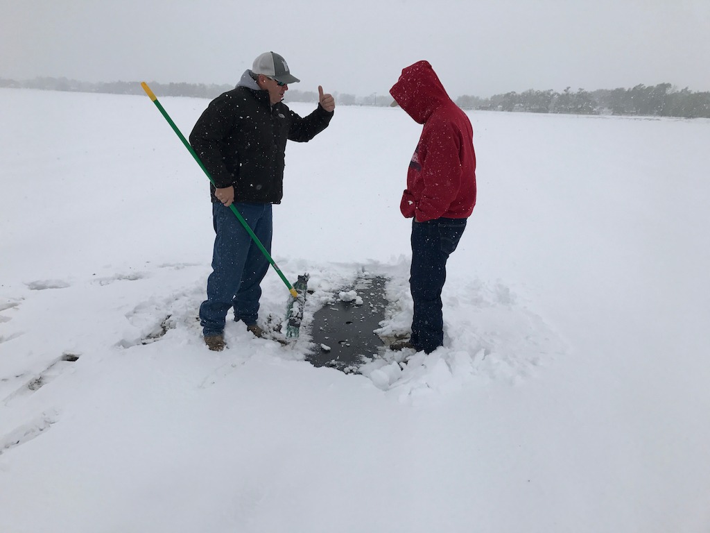 Matthew Proctor of Proctor Produce and Michael Hirakata, RFGA president and co-owner of Hirakata Farms, inspect a freshly-planted cantaloupe field by brooming the snow off the mulch to see if the cantaloupe seeds have sprouted. Seeds that haven't sprouted may make it through the snow and freezing temps, seedlings will likely be lost and need to be replanted.