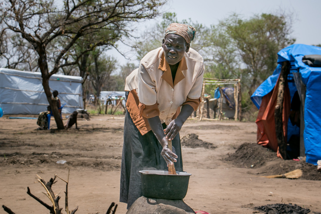 A woman cooks posho (maize flour) on an open fire in a settlement within Palorinya refugee camp.<br/><br/>Food is scarce as rations are not regualrly distributed in parts of the camp so people eat what they can. Some have brought bags of casava, maize, and flour with them, others have to forage for food in the bush. Photographer: Fabio Basone/MSF