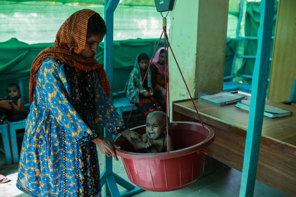 A mother puts her child in the weighing machine as part of the medical examination at the MSF run ambulatory therapeutic feeding centre (ATFC) at DHQ hospital in Dera Murad Jamali in Balochistan, Pakistan. Photographer: Sara Farid