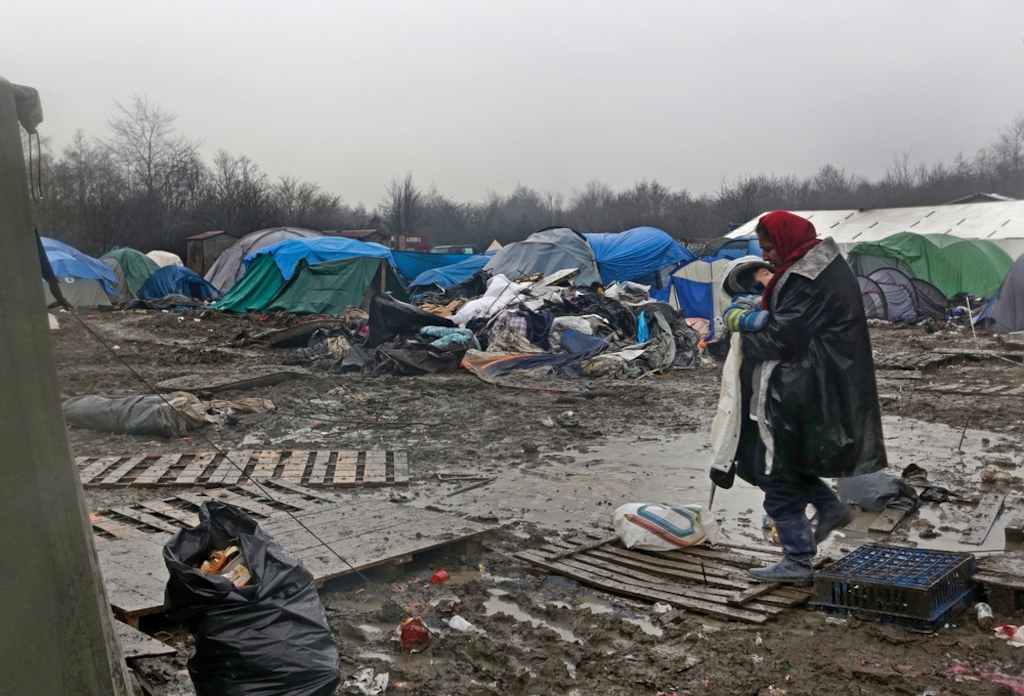 Herro, from Iraqi Kurdistan, carries her four-year-old son across the mud to her tent in the Grande Synthe refugee camp in Dunkirk, northern France. Photographer: Jon Levy/MSF