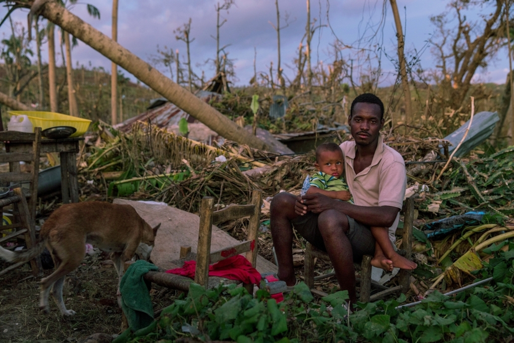 A man sits with his son, in the remains of their home, near Port Salut, in southwestern Haiti. Hurricane Matthew tore through the Caribbean on 4 October devastating large parts of the island. MSF teams used every means of transport, including donkeys, to bring medical aid to some of the more remote communities in the mountains, cut-off by damage to bridges and roads. Photographer: Andrew McConnell/Panos Pictures